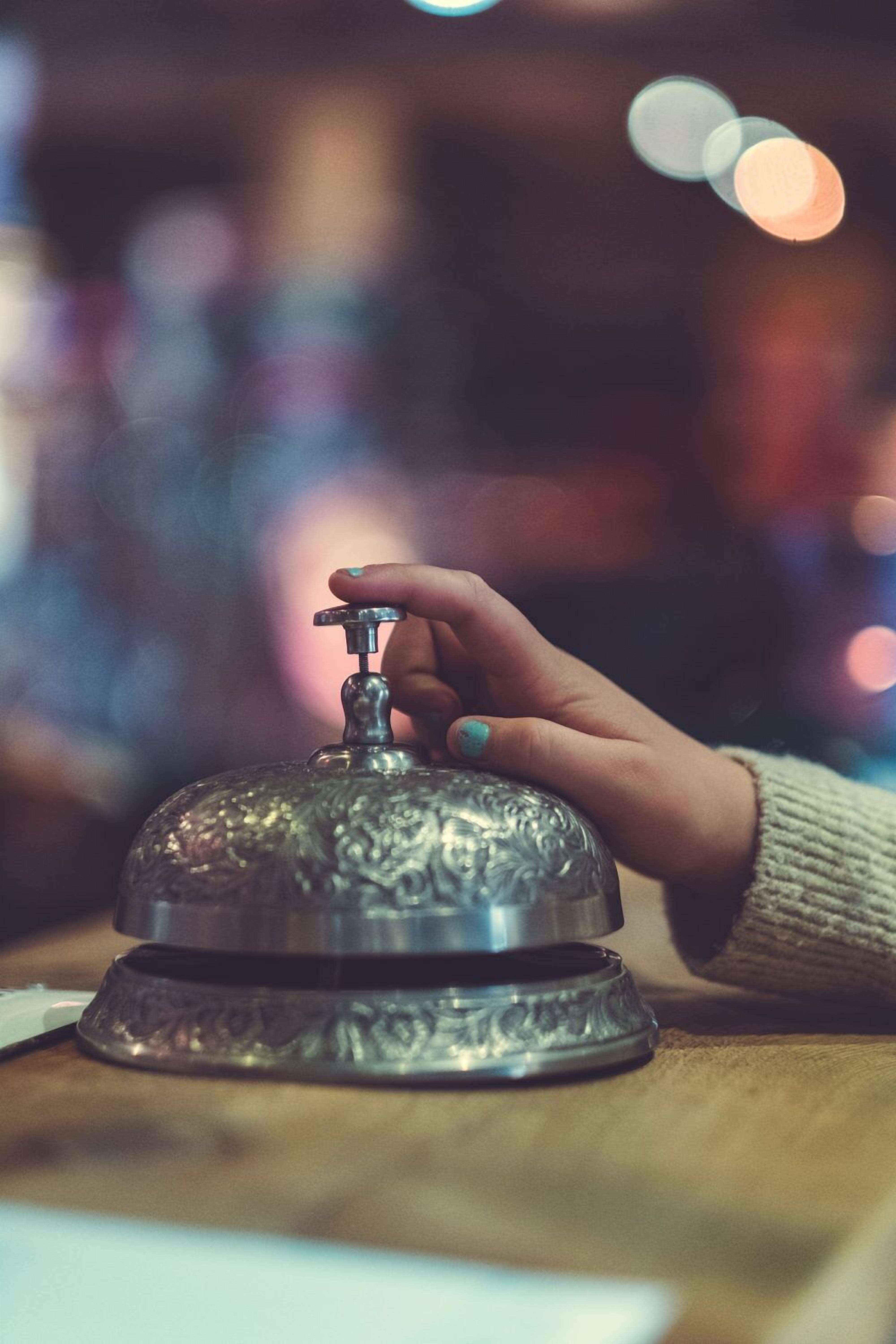 A hand adjusting a metallic, ornate bell on a wooden surface.