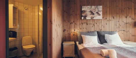 Una habitación con paneles de madera, una cama, una mesita de noche, un inodoro blanco y una zona de ducha.