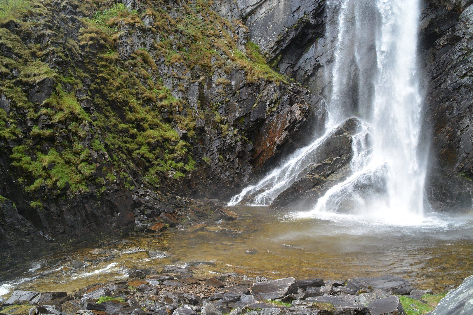 Una cascata che si getta da una parete rocciosa in una piccola pozza, circondata da rocce ricoperte di muschio.