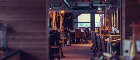 Ein Blick ins Restaurantinnere zeigt Holzwände, Tische, Stühle und einen Ausblick durch ein Fenster.