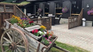 Een rustiek houten gebouw met rieten dak, zitplaatsen buiten en bloempotten.