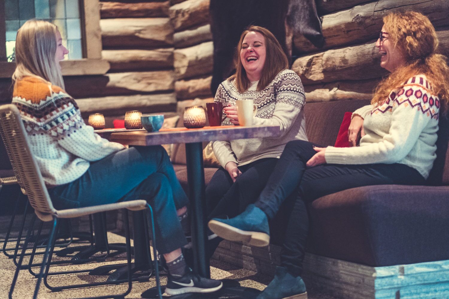 Three people seated around a table with candles and a mug, in a room with a rustic log wall.