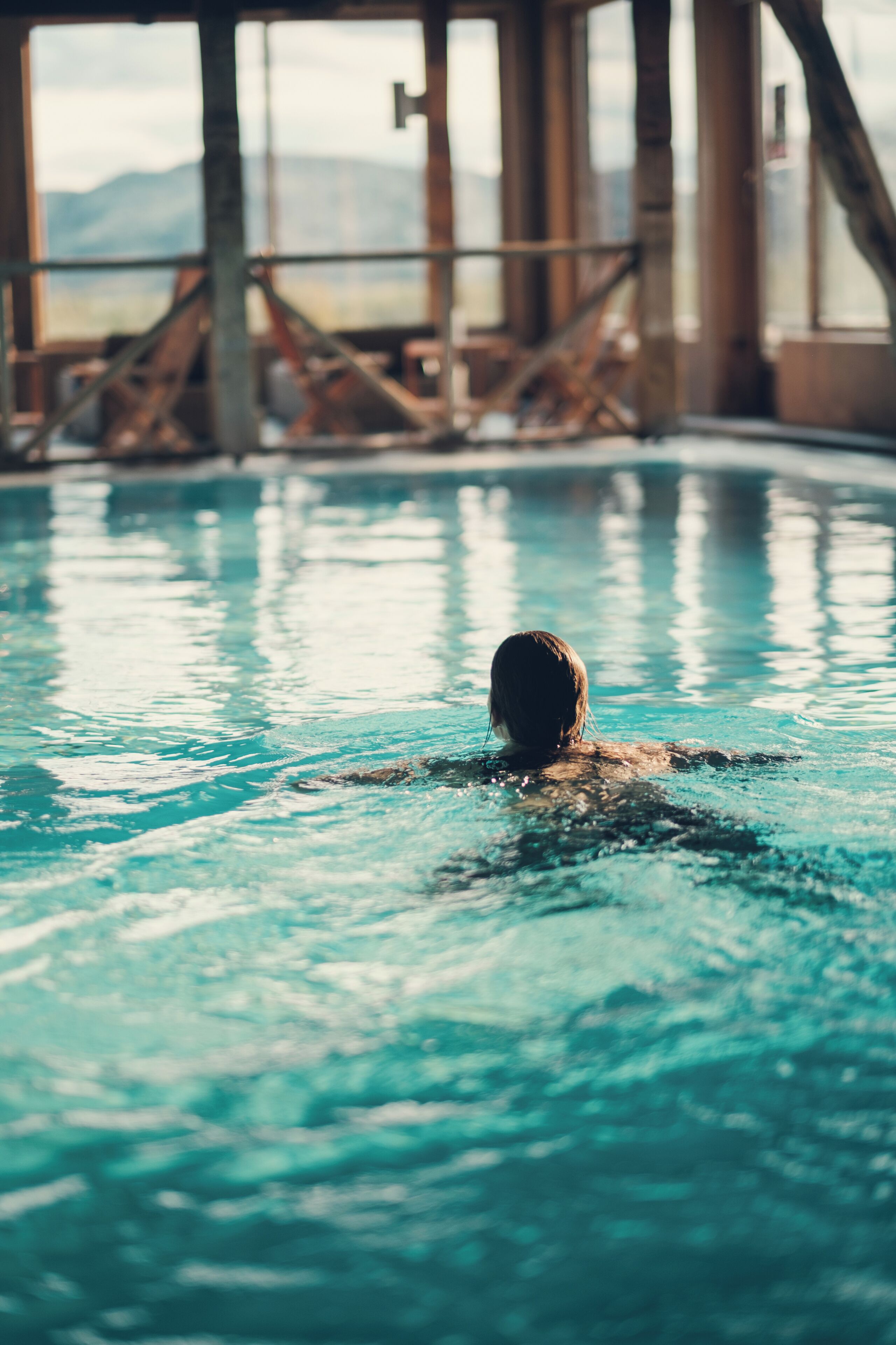 Una persona nuota in piscina con vista su un paesaggio montuoso e strutture industriali sullo sfondo.