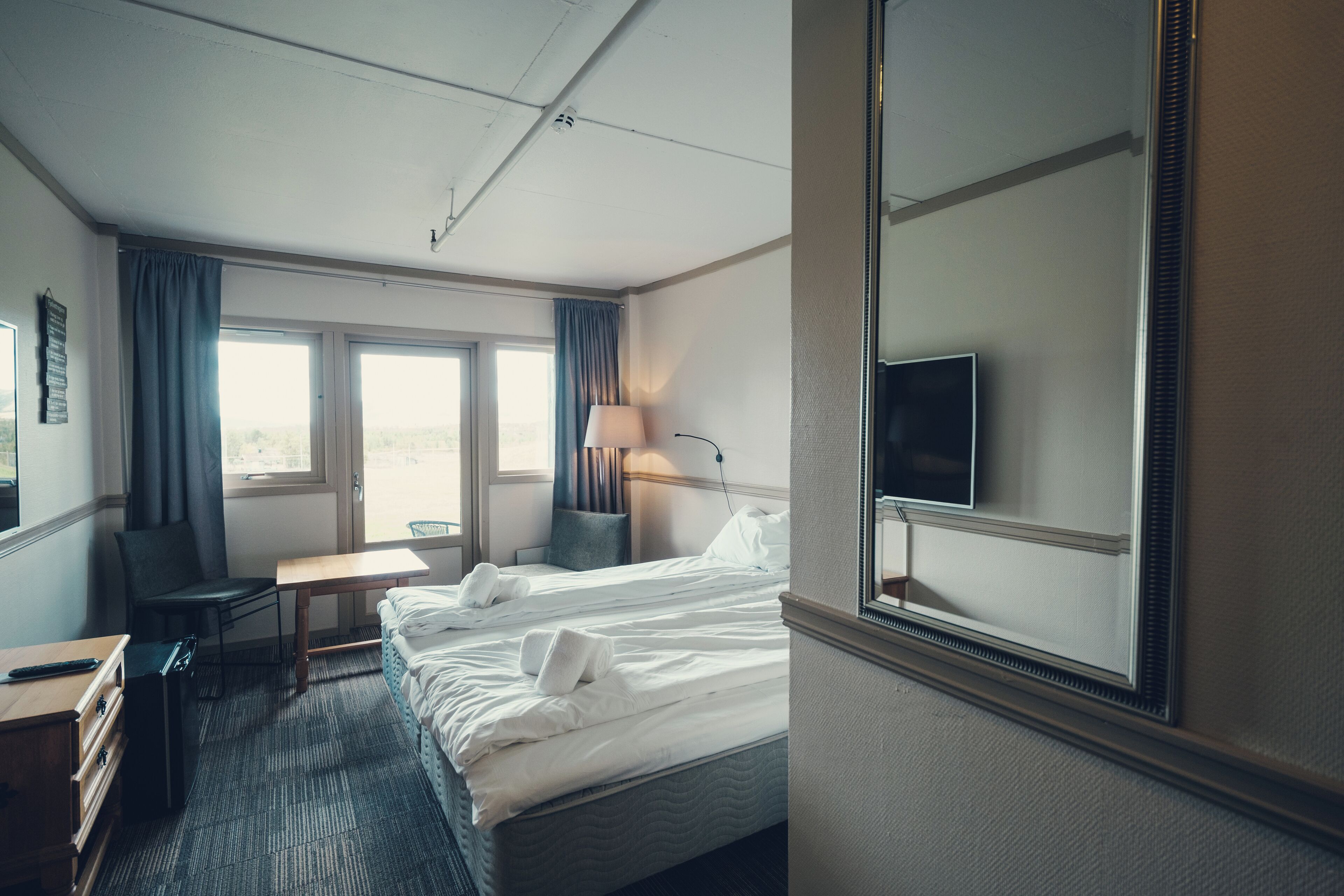 A hotel room with two beds, a desk, a chair, a TV, and a window with curtains.