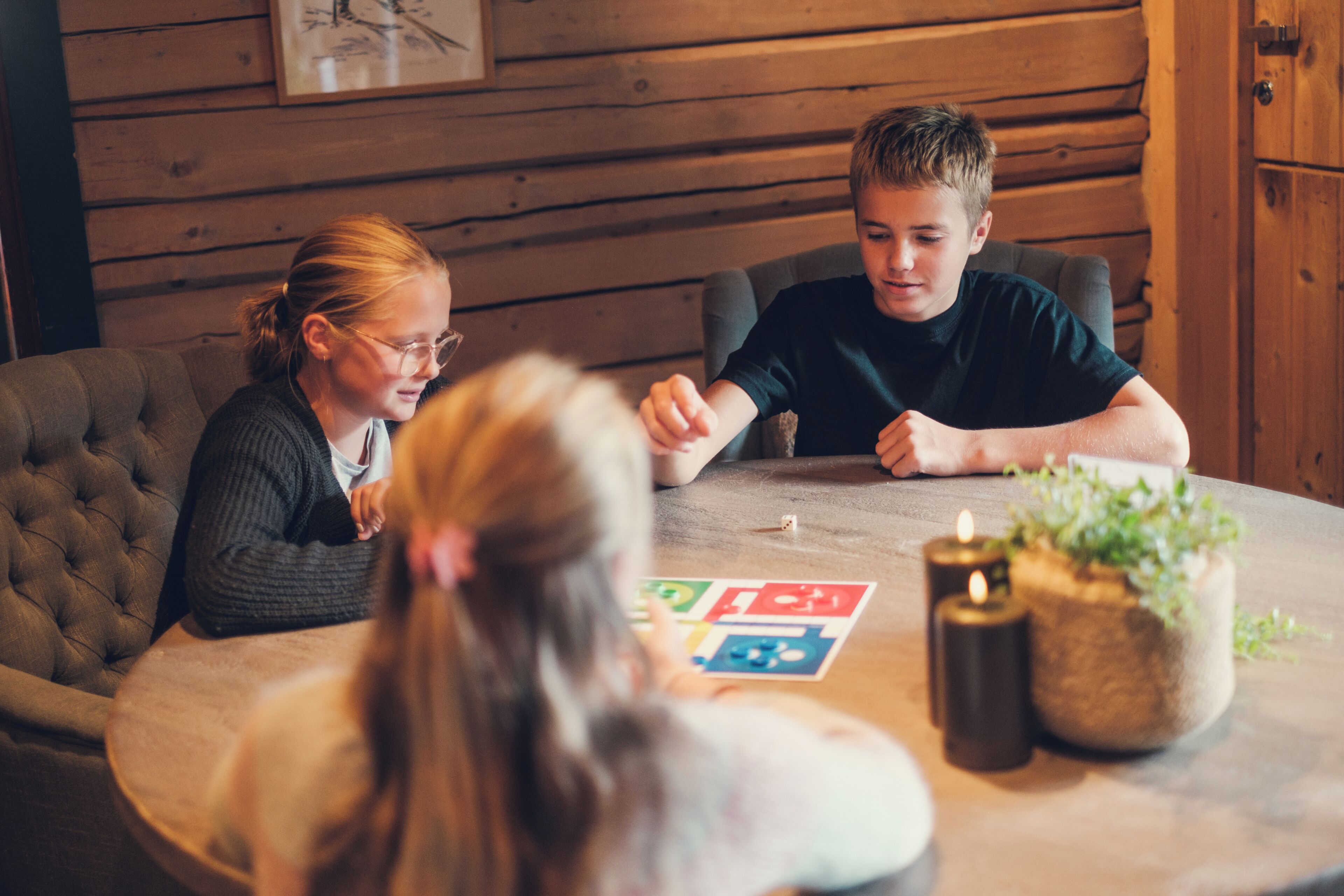A round wooden table with a board game, candles, and a potted plant.