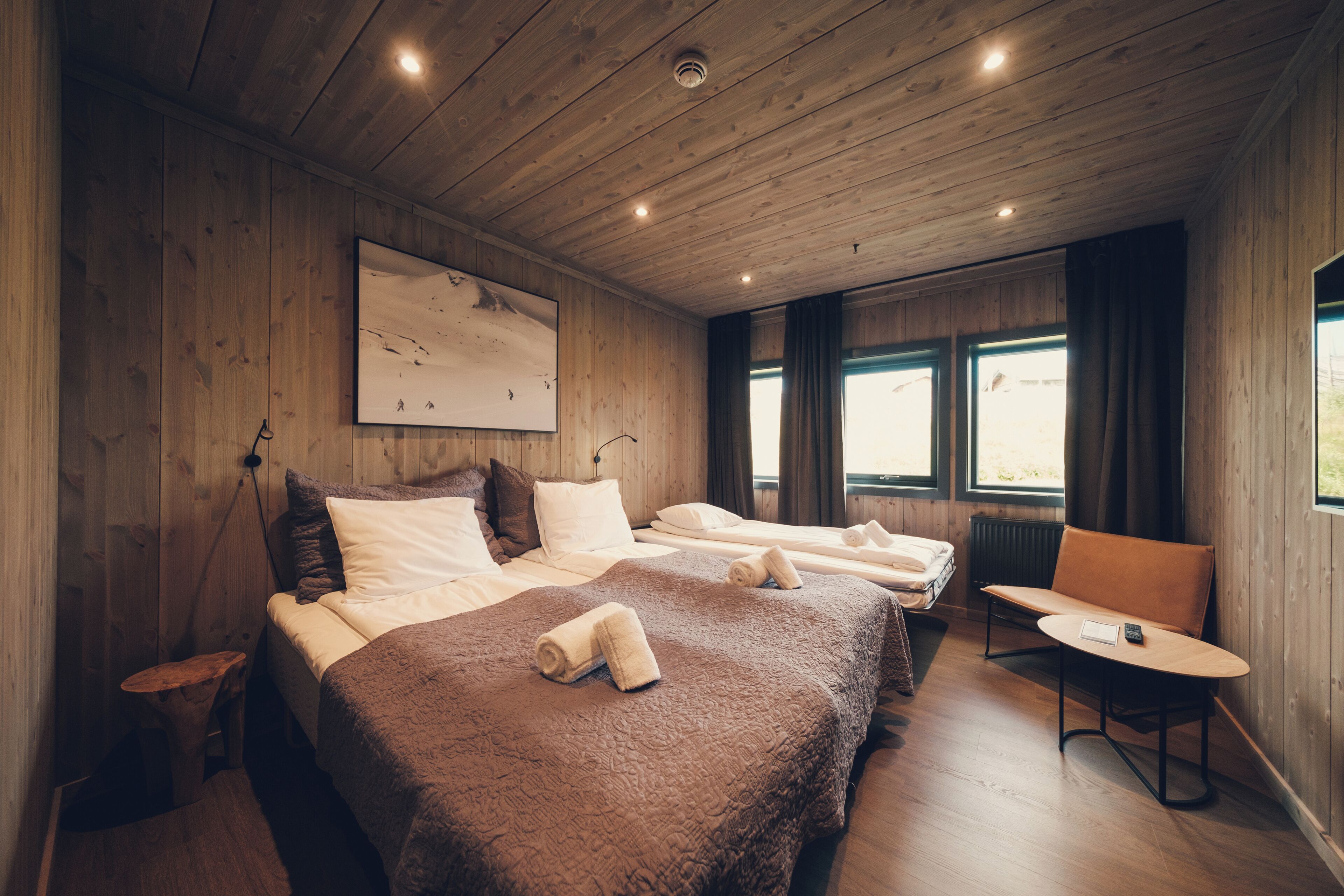 A wooden-paneled room with two beds, a small table, and a chair.