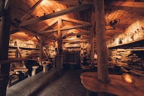 A rustic interior with wooden beams, stone walls, and a bar area with shelves of bottles.