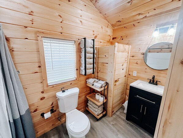 A wooden cabin bathroom with a toilet, sink, and shelves for towels. - Cozy tiny cabin in Petros -Windrock (Oliver Springs)