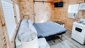 A compact wooden cabin room with a bed, a small table, a TV, and a kitchenette. - Cozy tiny cabin in Petros -Windrock (Oliver Springs)