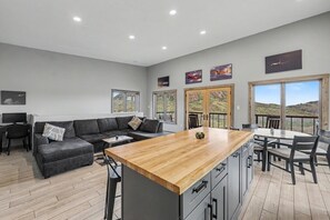 A modern kitchen with a wooden island, grey cabinetry, and a dining area with a view.