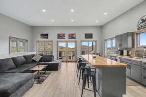 A modern kitchen with a central island, bar stools, and a dining area with a sofa and coffee table. - Infinite Skies Retreat • 727 Airplane Home (Terlingua)