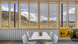 A room with a large window overlooking a rocky landscape, a white table with chairs, and a directional sign. - Infinite Skies Retreat • 727 Airplane Home (Terlingua)