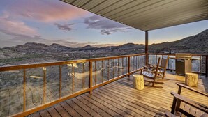 Una terraza de madera con barandilla de vidrio que da a un paisaje montañoso.