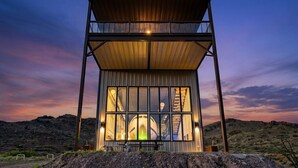 A modern, two-story glass building with a metal roof, set against a desert landscape at dusk. - Infinite Skies Retreat • 727 Airplane Home (Terlingua)