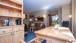Un espacio acogedor con mesa de comedor de madera, un sofá y una mesita de centro. Hay una zona de cocina con estufa y armarios.