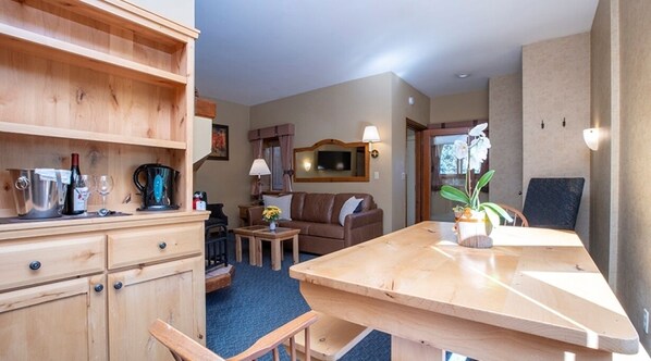 A cozy living area with a wooden dining table, a sofa, and a coffee table. There is a kitchen area with a stove and cabinets.