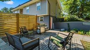 A residential backyard with a patio, outdoor furniture, a barbecue grill, and a wooden fence.