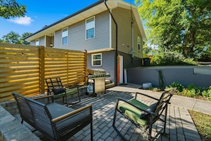 A residential backyard with a patio, outdoor furniture, a barbecue grill, and a wooden fence.