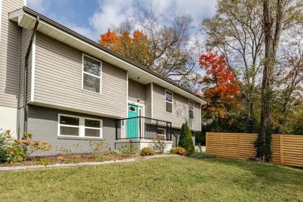 A two-story residential building with a front porch, a small front yard, and a wooden fence.