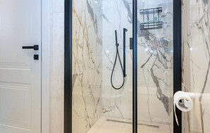 Eine Duschkabine mit Glas, eine Marmorwand, ein Handtuchhalter und ein Toilettenpapierhalter.