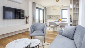 Ein modernes Wohnzimmer mit einem grauen Sofa, zwei Marmortischen und einem an der Wand befestigten Flachbildfernseher.