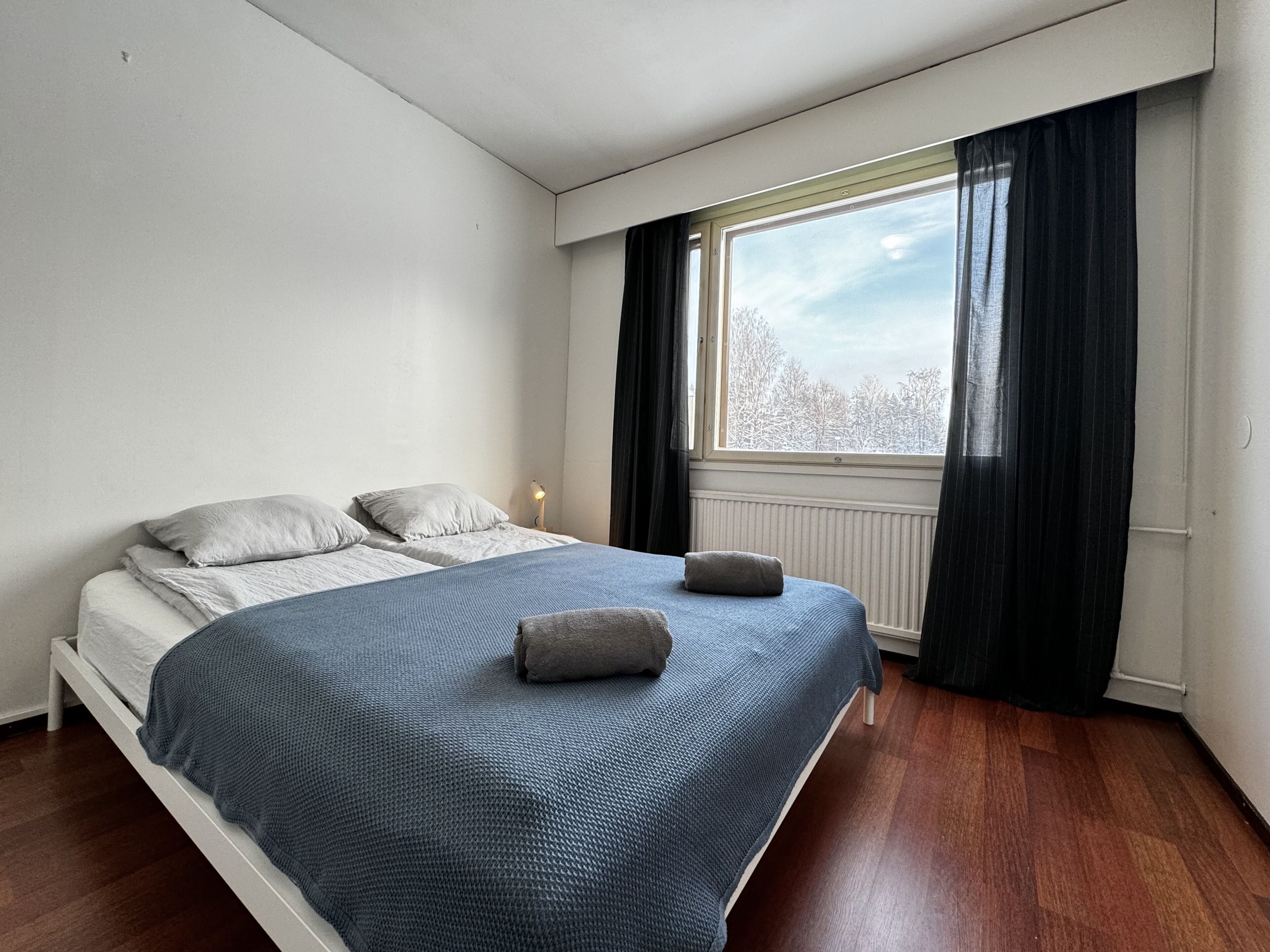 Ein Schlafzimmer mit einem großen Bett, einem Fenster mit Vorhängen und einer Heizung.