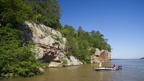 A boat on a calm river with rocky cliffs and dense greenery on the banks. - Full-Hookups, Free Laundry, Pet Park, Near Mt. Nebo and Lake Dardanelle- Adventure Awaits! (Dardanelle)