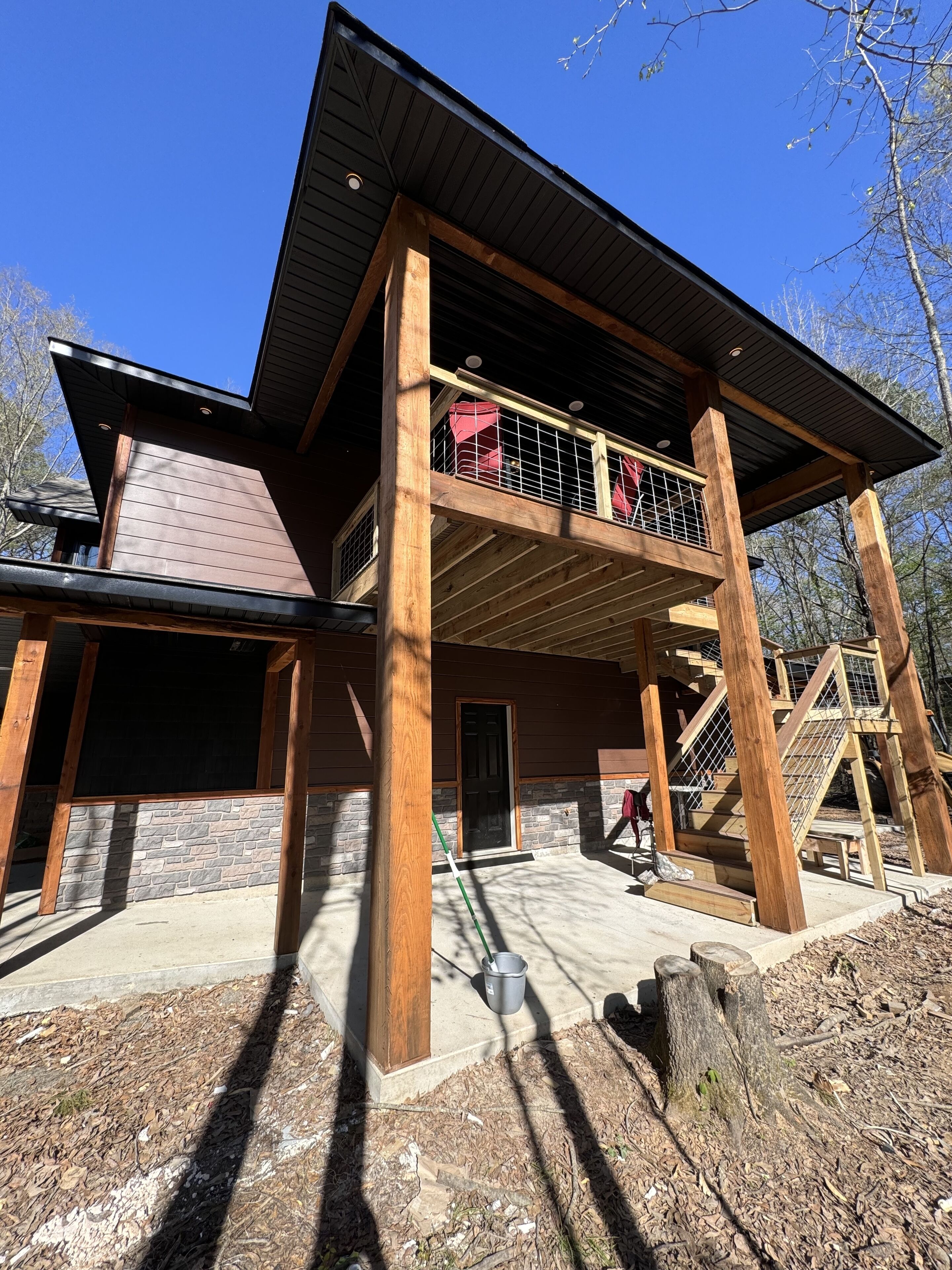 A two-story wooden house with a balcony, stone foundation, and a clear sky.