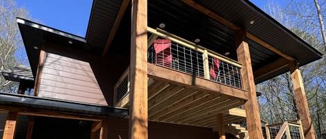 A two-story wooden house with a balcony, stone foundation, and a clear sky.