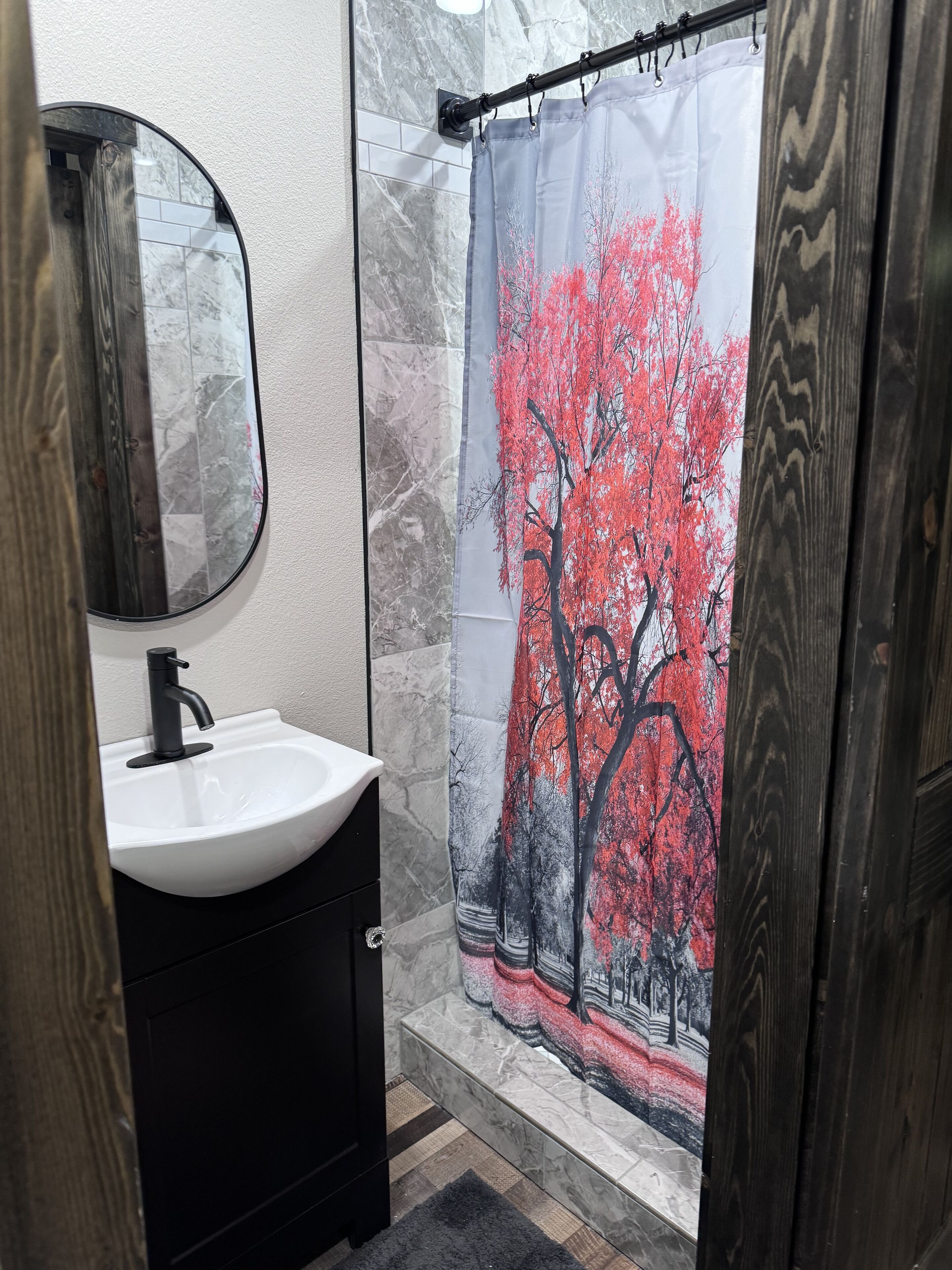 Un baño con un lavamanos blanco, un mueble negro y una cortina de ducha con un diseño de árbol rojo.