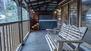 A wooden deck with a swing, a hot tub, and a covered area with a view of trees. - A~Bears Den- Pet Friendly, Hot Tub, 2 King Suites, Minutes to GSMNP! (Townsend)