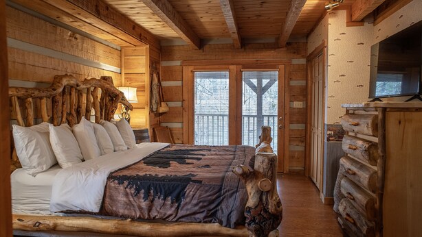A log cabin bedroom with a large bed, wooden walls, and a rustic design. - A~Bears Den- Pet Friendly, Hot Tub, 2 King Suites, Minutes to GSMNP! (Townsend)