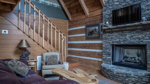 A cozy living room with a stone fireplace, wooden staircase, and a comfortable seating area. - A~Bears Den- Pet Friendly, Hot Tub, 2 King Suites, Minutes to GSMNP! (Townsend)