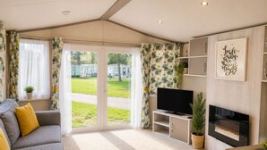A living room with a sofa, TV, fireplace, and a view of a park. - Bird Lake Pastures 2 Bedrooms 2 Baths  (Northampton)