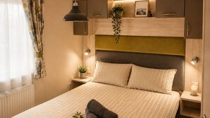 A bedroom with a bed, bedside tables, a hanging plant, and a ceiling light. - Bird Lake Pastures 2 Bedrooms 2 Baths  (Northampton)
