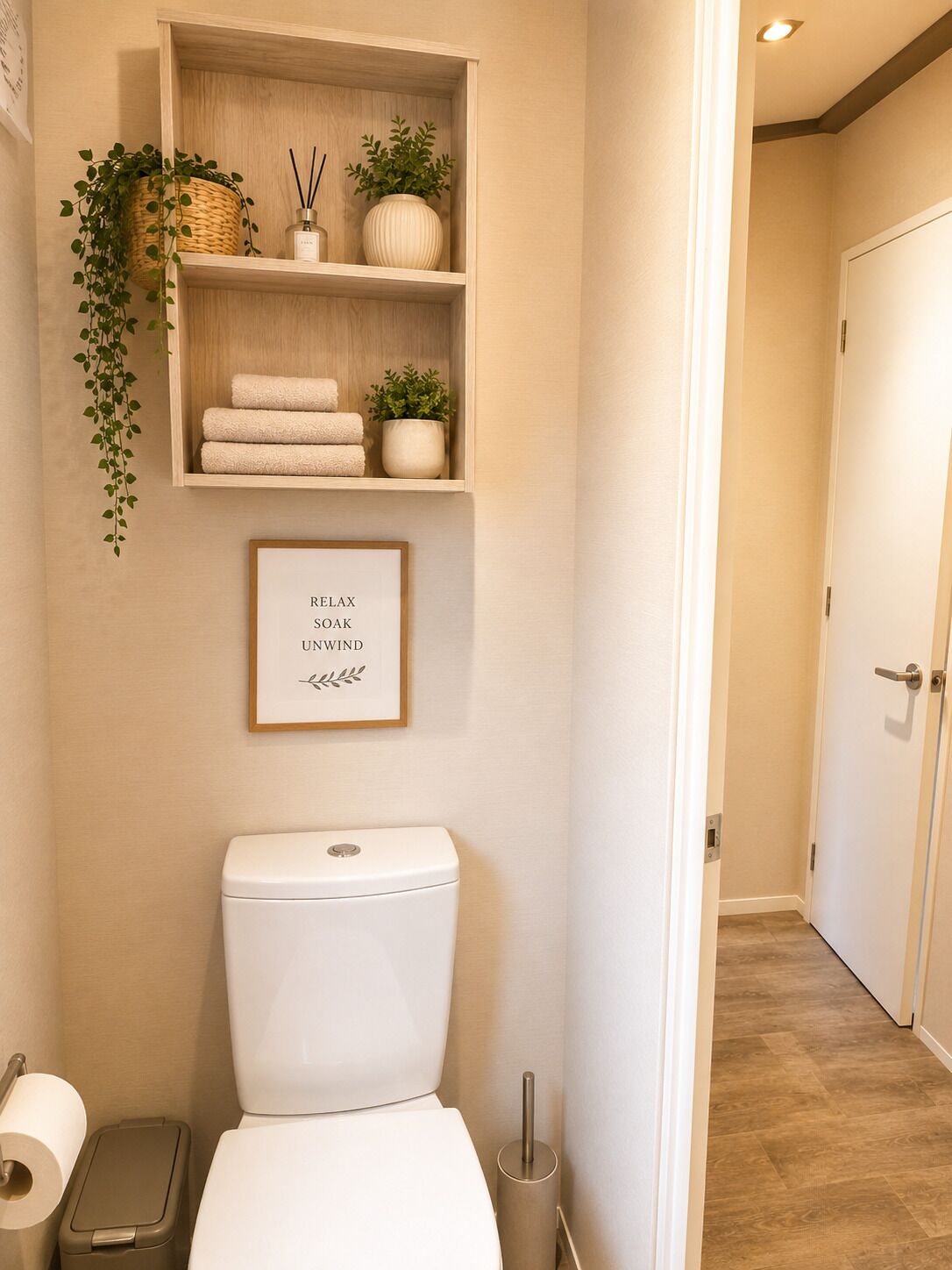 A bathroom with a toilet, a shelf with towels and plants, a framed sign, and a roll of toilet paper.
