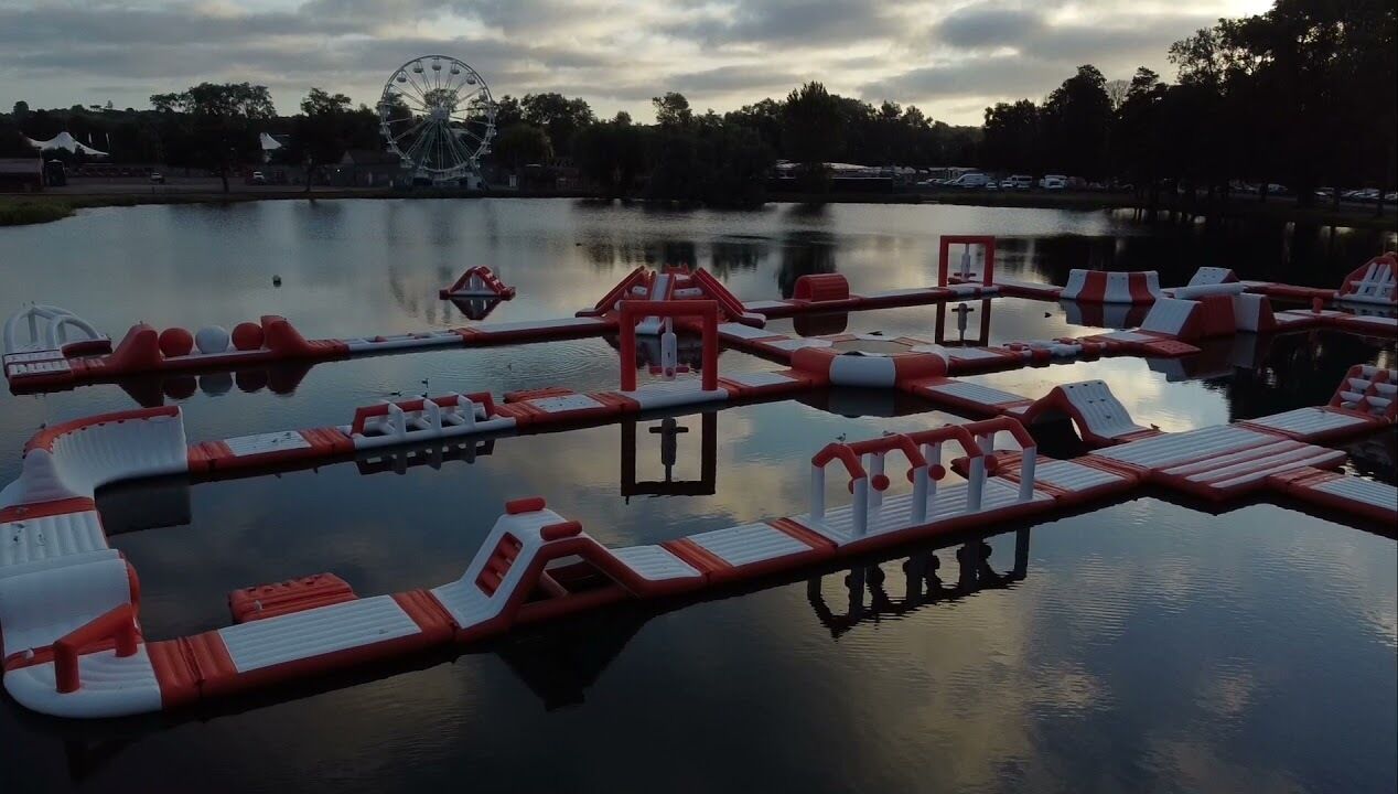 Un parc aquatique avec des structures de jeux gonflables et une grande roue en arrière-plan.