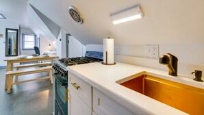 Una cocina con muebles blancos, estufa de acero inoxidable, banco de madera y un ventanal.