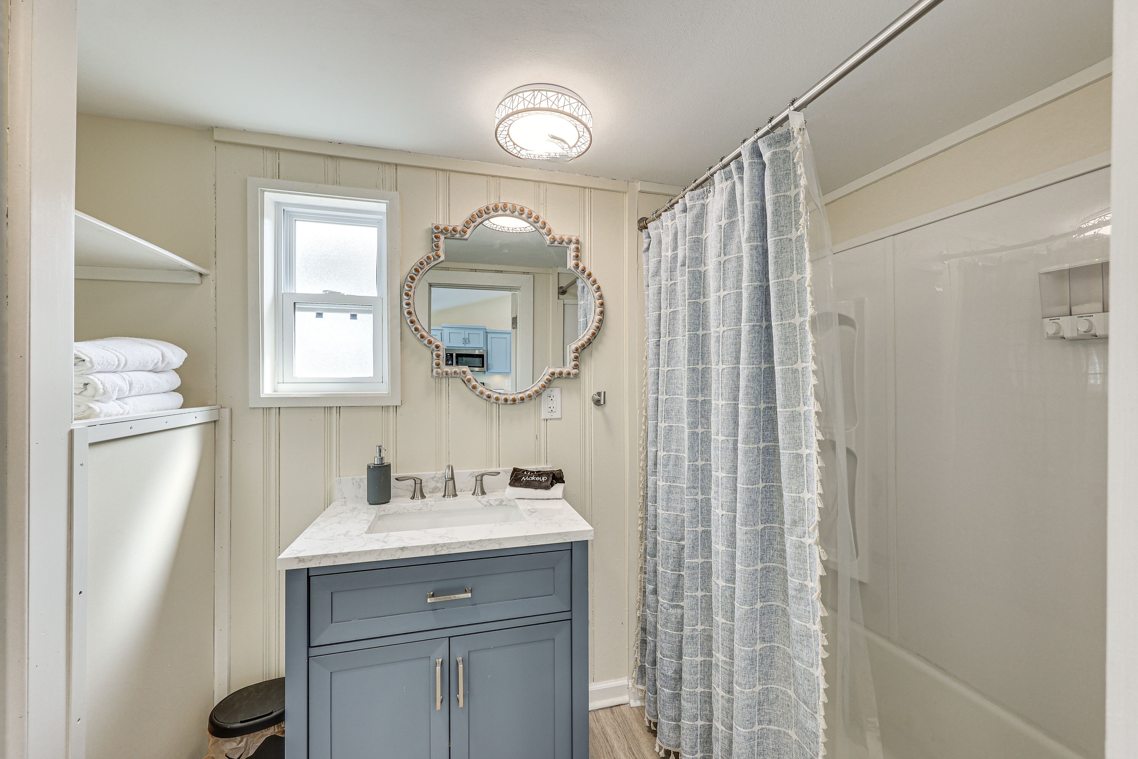 Une salle de bain avec un meuble-lavabo, un miroir avec un cadre décoratif, un rideau de douche et une fenêtre.