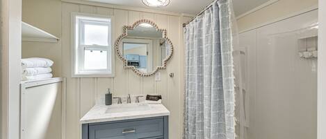 Une salle de bain avec un meuble-lavabo, un miroir avec un cadre décoratif, un rideau de douche et une fenêtre.
