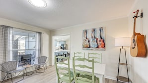 Un comedor con una mesa y sillas blancas, un cuadro de una guitarra y una lámpara.