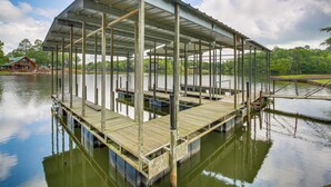 Un muelle techado con techo metálico y tablas de madera, que se adentra en una masa de agua tranquila.