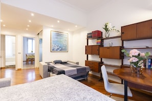 A bedroom with a bed, a desk, a chair, a bookshelf, and a painting.