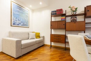 A room with a sofa, a wooden desk, a bookshelf, and a painting on the wall.