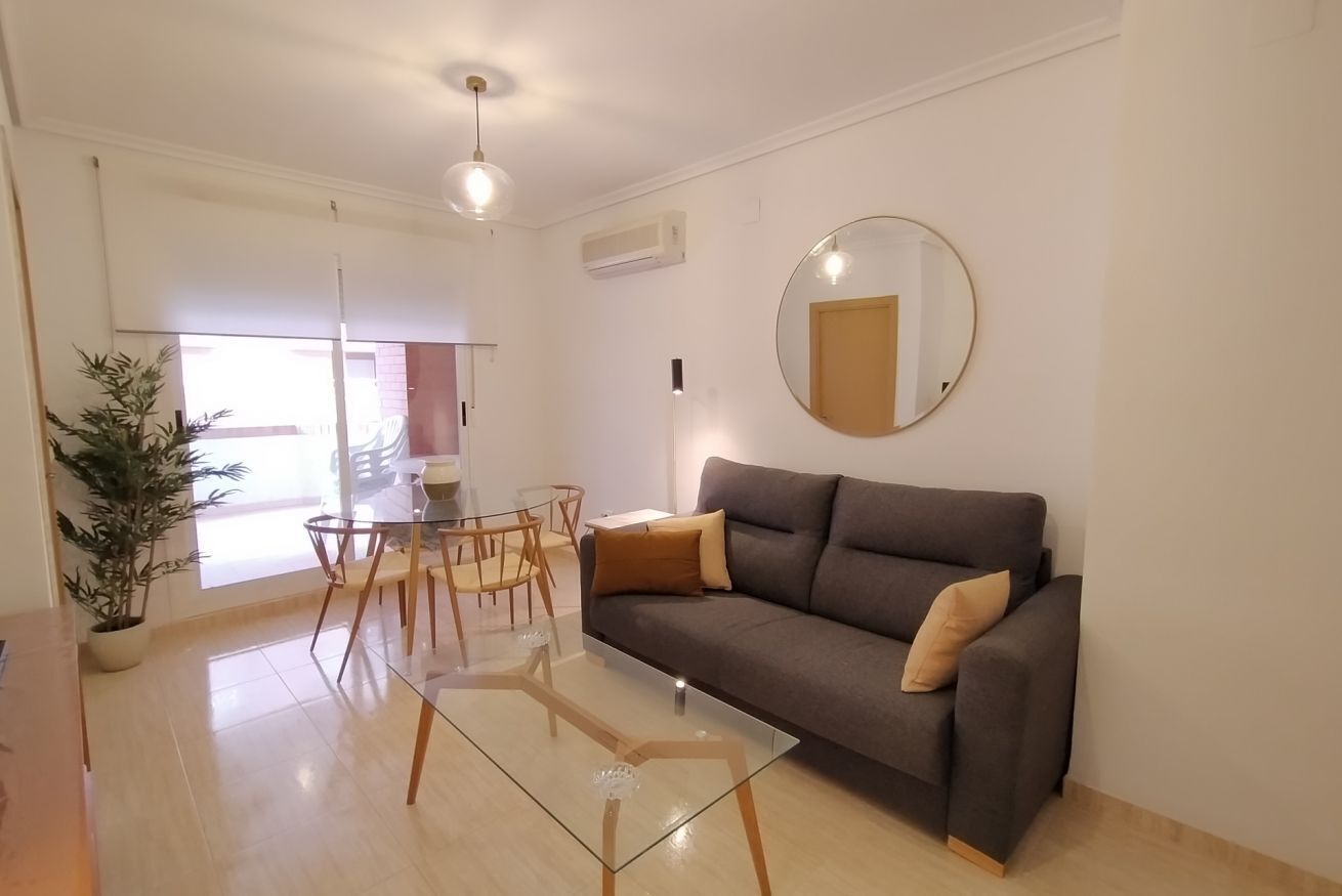 A modern living room with a sofa, a glass coffee table, and a dining area with chairs and a table.