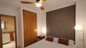 Habitación de hotel con cama, ventilador de techo, mesita de noche con lámpara, armario de madera y panel de pared a rayas.