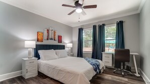 A bedroom with a bed, bedside tables, a desk, a chair, a ceiling fan, and artwork on the wall. - Charlotte Pet Friendly 3BR Chateau • Hot Tub • Mini Golf • Fire Pit • SouthPark (Charlotte)