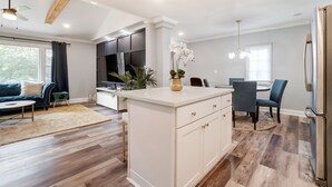 A modern kitchen with a central island, a dining area with blue chairs, and a living room with a blue sofa. - Charlotte Pet Friendly 3BR Chateau • Hot Tub • Mini Golf • Fire Pit • SouthPark (Charlotte)