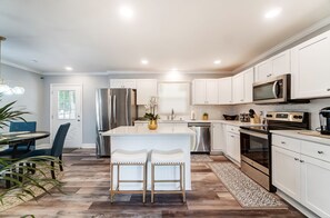 A modern kitchen with white cabinetry, stainless steel appliances, and a central island with bar stools. - Charlotte 3BR Getaway | Hot Tub • Mini Golf • Pet-Friendly • Fire Pit (Charlotte)