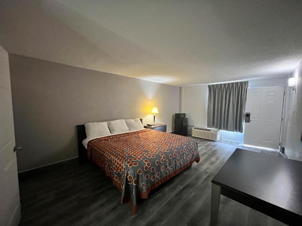 Habitación de hotel con cama, mesita de noche, lámpara y vistas al exterior.